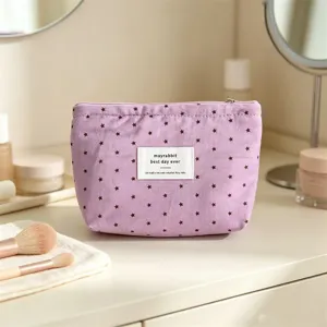 Dettaglio borsa cosmetica in tessuto viola con stampa di stelle ed etichetta frontale.