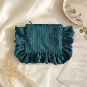 Corduroy cosmetic bag detail showing dark green fabric texture, zipper, and ruffled design.