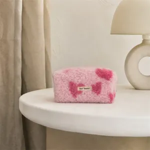 Gedetailleerde close-up van een roze pluche make-uptas met hartjesmotief op een witte tafel.