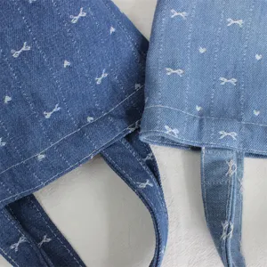 Primer plano del detalle del bolso de mezclilla con tela azul, lazos blancos y costuras.