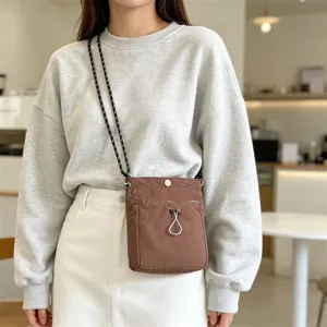 Detailansicht der braunen Nylon Mini Umhängetasche getragen im lässigen Innenbereich Modell.