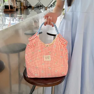 Gros plan d'un sac cabas en toile à carreaux rouges avec nœuds et anses bleues.