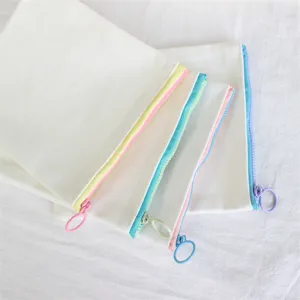 Close-up detail of simple white canvas pencil case with colorful pastel zippers and round pull ring.