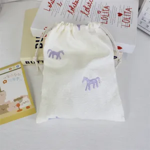 Close-up detail shot of white drawstring bag featuring cute embroidered purple horse pattern.