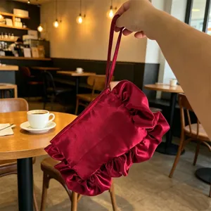 Detalle de bolso de mano de satén plisado con volantes, diseño elegante con correa de muñeca.