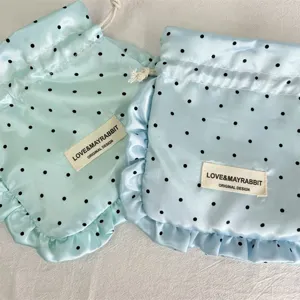 Satin polka dot drawstring pouch with ruffle detail, perfect for jewelry and cosmetic storage.