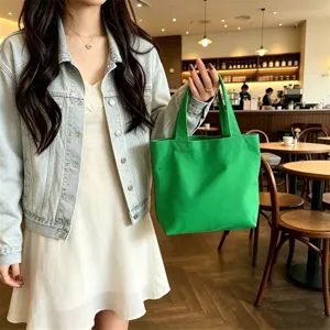 Close-up detail shot of a stylish mini nylon tote bag in vibrant green held in cafe.