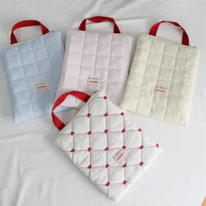 Quilted laptop sleeve detail showing soft pastel colors, red handles, and neat stitching.