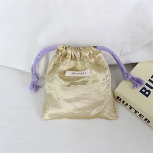 Close-up van het gouden satijnen sieradenzakje met paarse koorden en een klein label.