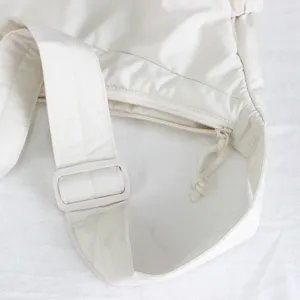 Primo piano della tracolla della borsa bianca, fibbia regolabile, zip e morbida consistenza.