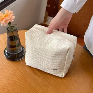 Detailaufnahme der strukturierten Beigen Kosmetiktasche mit Reissverschluss auf Tisch.
