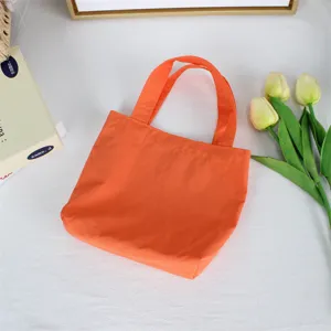 Detail view of a vibrant orange mini nylon tote bag styled with fresh tulips on white background.