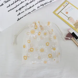 Close-up detail of sheer white drawstring pouch featuring cute yellow and white daisy embroidery.