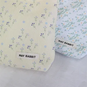 Corduroy floral cosmetic bag detail view, soft fabric texture with woven label accent.