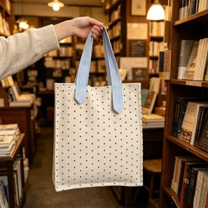Vista dettagliata della borsa in tela, borsa beige con stelle nere e manici a righe blu.
