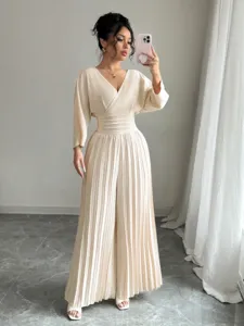 Elegant beige V-neck short sleeve pleated wide leg jumpsuit detail view in bright indoor scene.