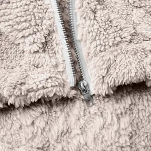 Nahaufnahme der Textur von weichem, beigen Fleece-Jackenstoff und Metallreißverschluss.
