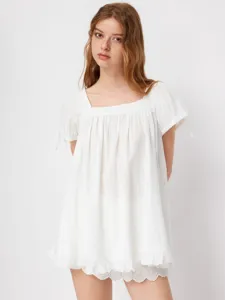 Primo piano di una blusa bianca con scollo quadrato, orlo volant e graziosi lacci sulle maniche.