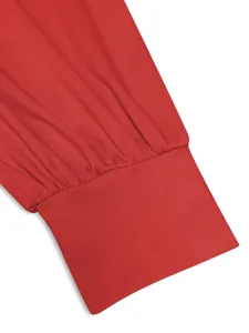 Dettaglio dell'abito a manica lunga rosso con polsino a lanterna arricciato e tessuto plissé