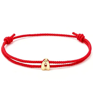 Red braided rope bracelet close-up with gold letter A charm, simple couple jewelry design.
