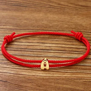 Close-up detail view of the red braided rope bracelet featuring a polished gold letter pendant.