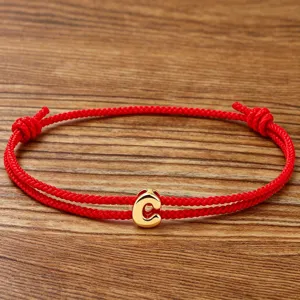 Detailed view of the red braided string bracelet with a gold letter C pendant in close up.