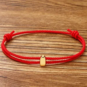 Detailed shot of a minimalist red string braided bracelet featuring a sleek gold bead pendant.