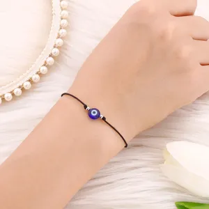 Gros plan sur un bracelet cordon noir avec une perle oeil bleu protecteur et des breloques.