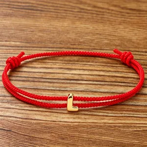 Red rope letter bracelet detail shot, minimalist gold initial charm woven couple jewelry.