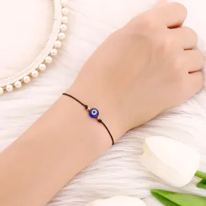 Bracelet cordon noir avec perle œil bleu et détails dorés vue rapprochée de détail.