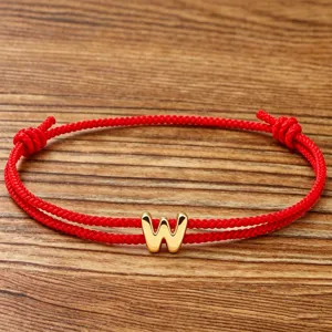 Close-up of gold letter W charm on red woven string bracelet, stylish minimal wear.