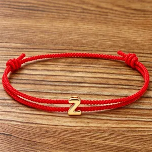 Red braided rope bracelet detail featuring a shiny gold letter Z charm, elegant couple jewelry.