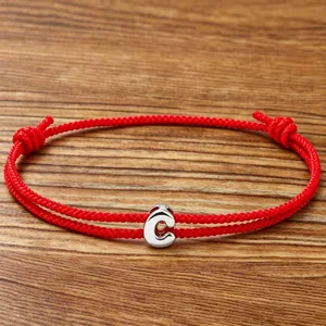 Close-up detail of the red braided rope bracelet featuring a silver letter C charm.