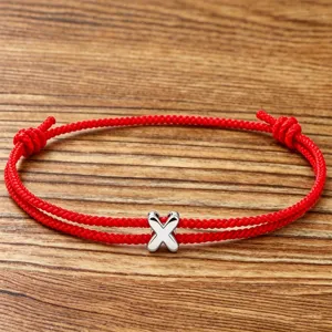 Close-up detail of the red braided cord bracelet featuring a shiny silver letter X charm.