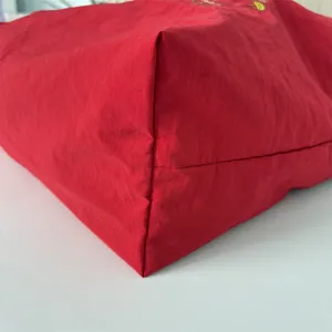 Vista detallada de bolso tote de tela roja que muestra costuras de fondo y textura de calidad.