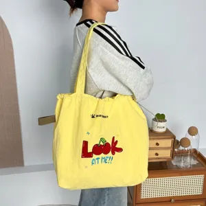 Vista detallada del bolso tote de lona amarilla con bordado de cerezas y correa cómoda.