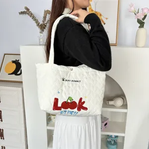 Detailed view of white quilted tote bag with cute cherry embroidery and heart pattern.