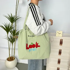 Detalle de bolso tote de lona verde, con bonito bordado de cerezas y cierre de cordón ajustable.