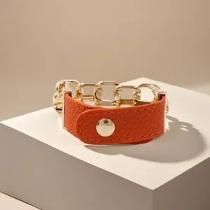 Nahaufnahme eines orangefarbenen Lederarmbands im Punk-Stil mit goldener Kette