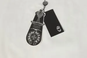 Close-up detail of Chrome Hearts and CDG brand hang tags on white cotton T-shirt fabric