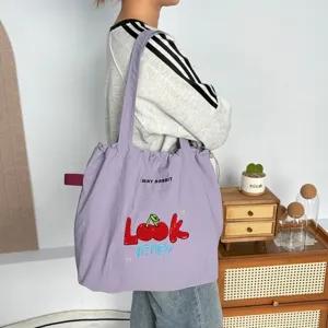 Vista detallada del bolso tote de lona morada con bordado de cerezas y cordón ajustable.