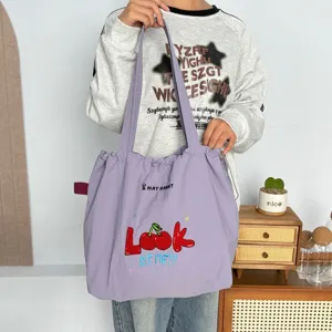 Vista detallada del bolso tote de lona morada con bordado de cerezas y cierre de cordón.
