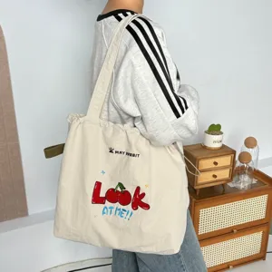 Vista detallada del bolso tote de lona con bonito bordado de cerezas y cordón ajustable.