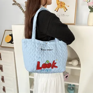 Close-up of light blue quilted heart tote bag with cute cherry embroidery and shoulder straps.