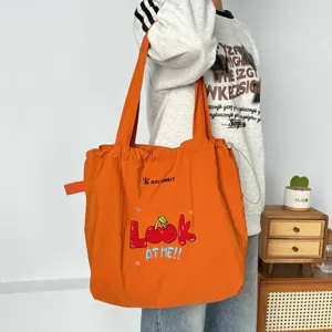 Detalle del bolso tote de lona naranja con bonito bordado de cerezas y cierre de cordón práctico.