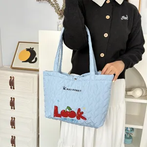 Detail view of a cute light blue quilted heart tote bag with cherry graphic and letters.