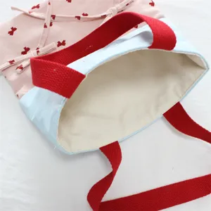 Detailansicht der Segeltuchtasche mit Farbdick-Design, roten Griffen und süßer Schleife.