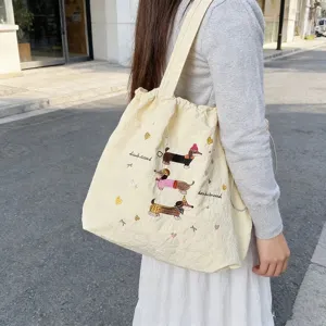 Dettaglio di una borsa tote in tela beige con simpatici bassotti ricamati sopra.