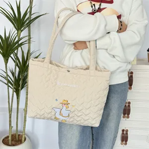 Gedetailleerd overzicht van beige gewatteerde tote tas met eend borduursel en ruime capaciteit.