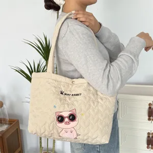 Gedetailleerd overzicht van beige gewatteerde shopper met schattig varkensborduurwerk.